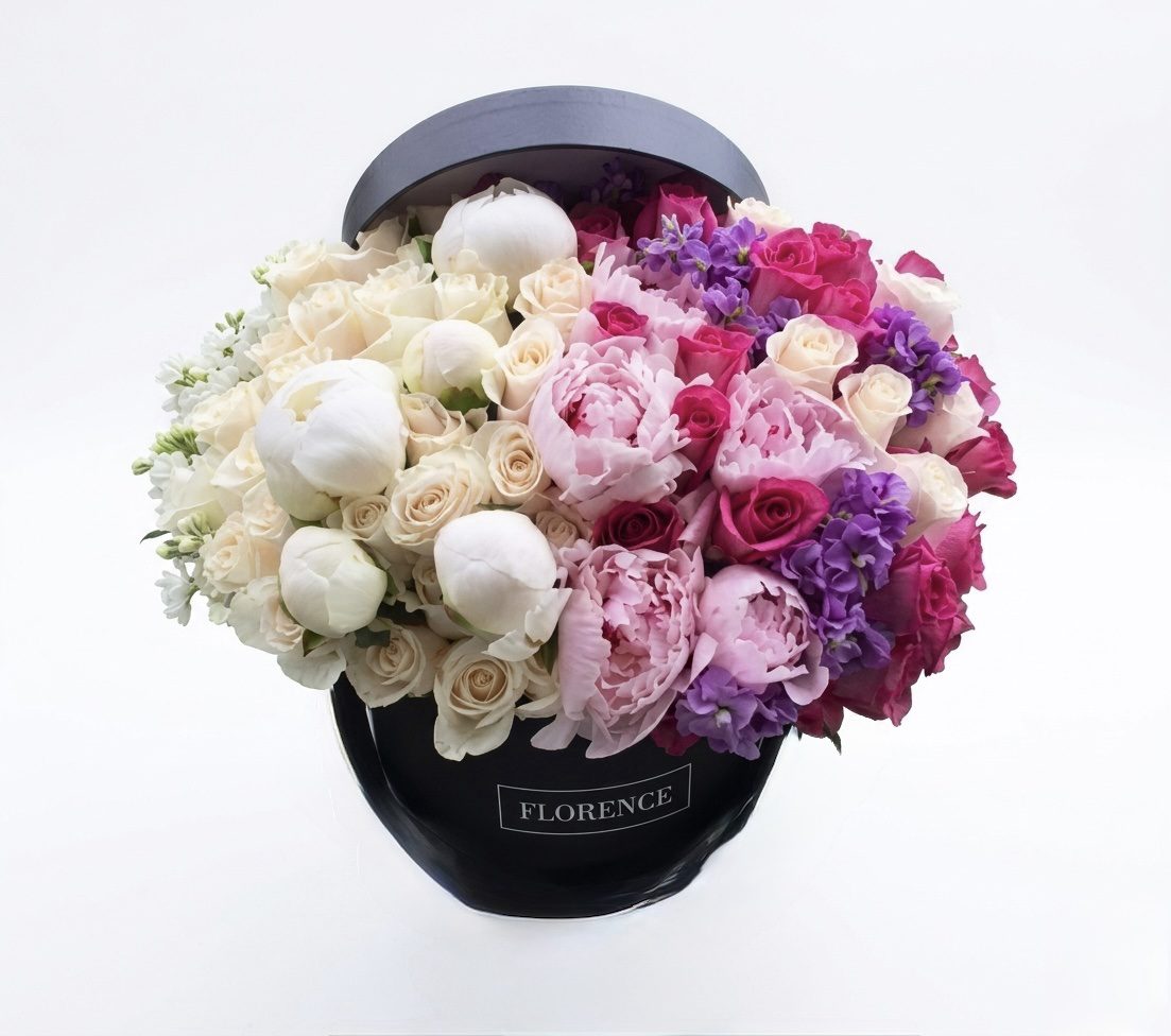 A black hatbox labeled FLEUR Collection #134 overflows with white, cream, pink, and purple roses and peonies, highlighting the elegance of Orange County Flowers against a plain white background.