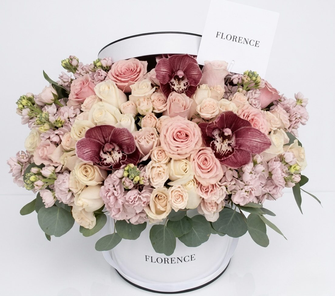 A white hatbox labeled FLEUR Collection #82 displays an elegant mix of blush pink and cream roses, pale purple blooms, and burgundy orchids—highlighting the timeless beauty of Orange County Flowers, with a matching card included.