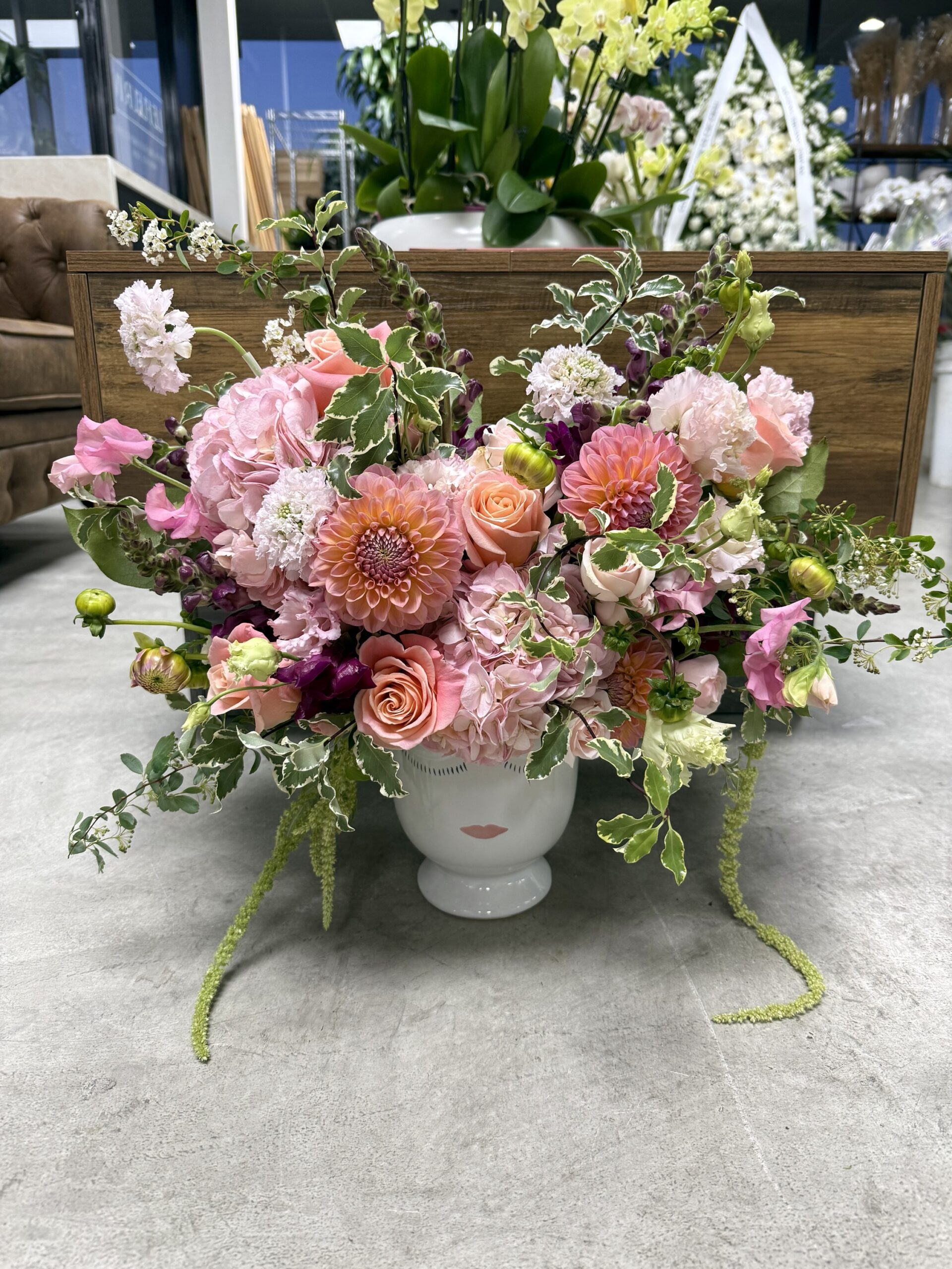 The Fiore Daydream - Ceramic vase is filled with pink dahlias, roses, and greenery, displayed on a gray floor in a modern floral shop.