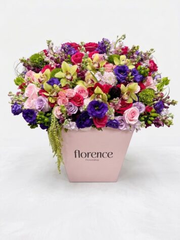A pink box labeled “Citrus Blooms - Grand Flower Box” holds a large, colorful bouquet with pink roses, purple lisianthus, green orchids, and mixed greenery, arranged against a plain white background.